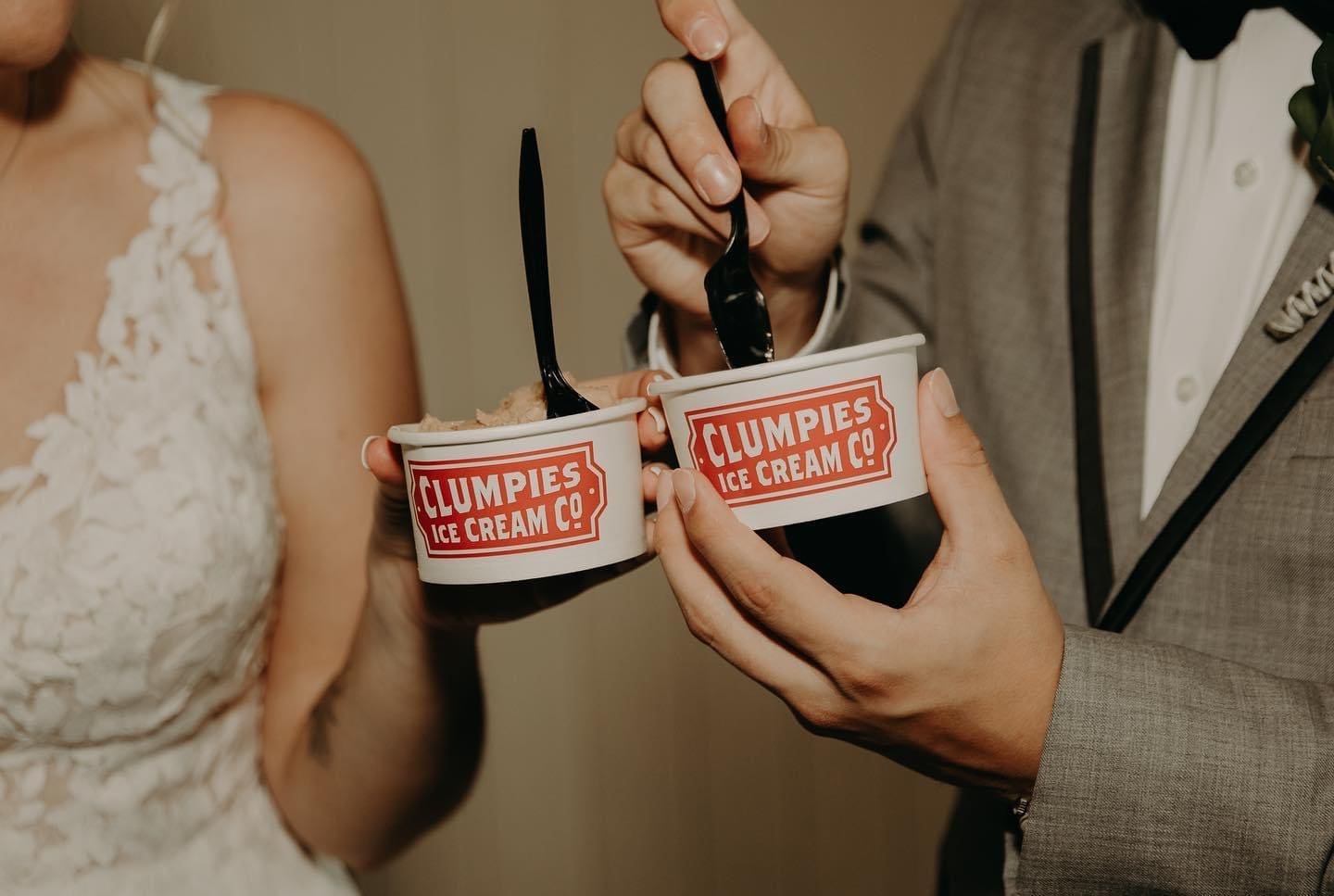 Bride and groom enjoying ice cream cups from Clumpies Ice Cream during their wedding reception, capturing a fun and candid late-night wedding dessert moment.