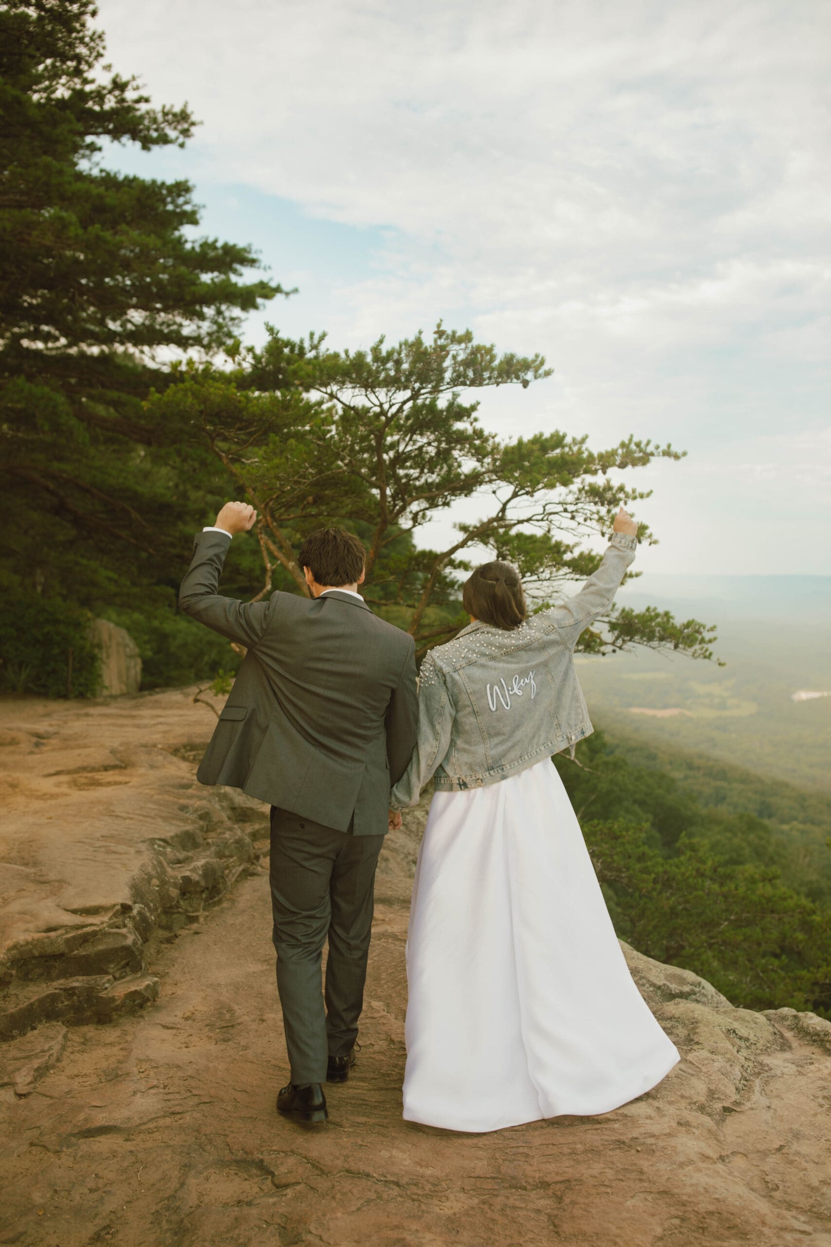 Bride and groom walking hand in hand along a scenic mountain overlook after their wedding ceremony, capturing an adventurous East Tennessee elopement moment at sunset.